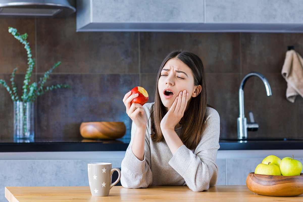common dental problems (1) woman holding jaw after biting into apple experiencing common dental problems