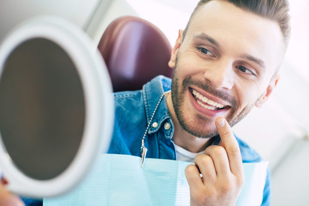 man smiling in mirror after dentist treating a chipped tooth